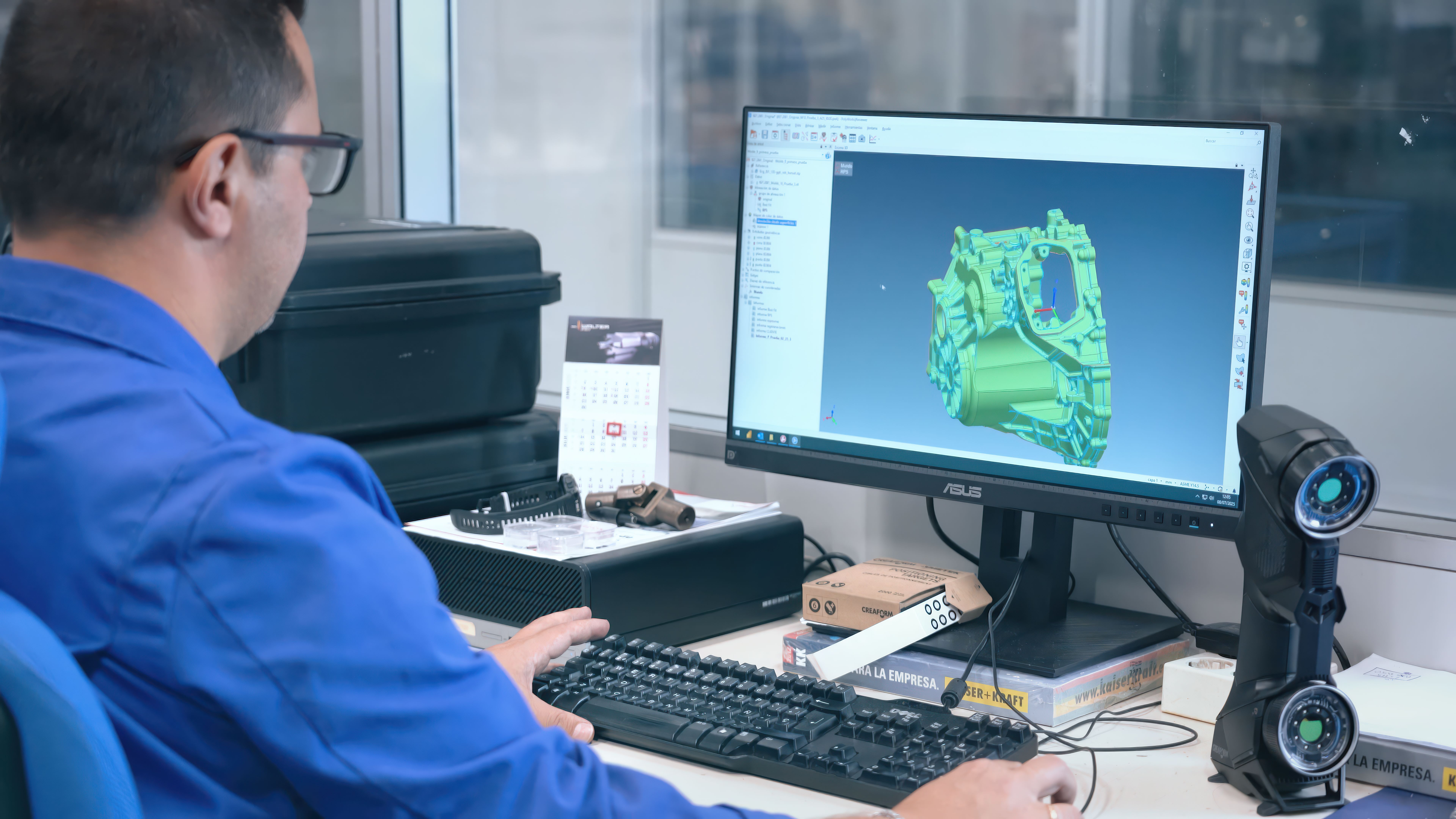 Martinrea Honsel employee sitting at a desk in front of a computer displaying a complex casting in PolyWorks with a HandySCAN BLACK scanner on the desk.