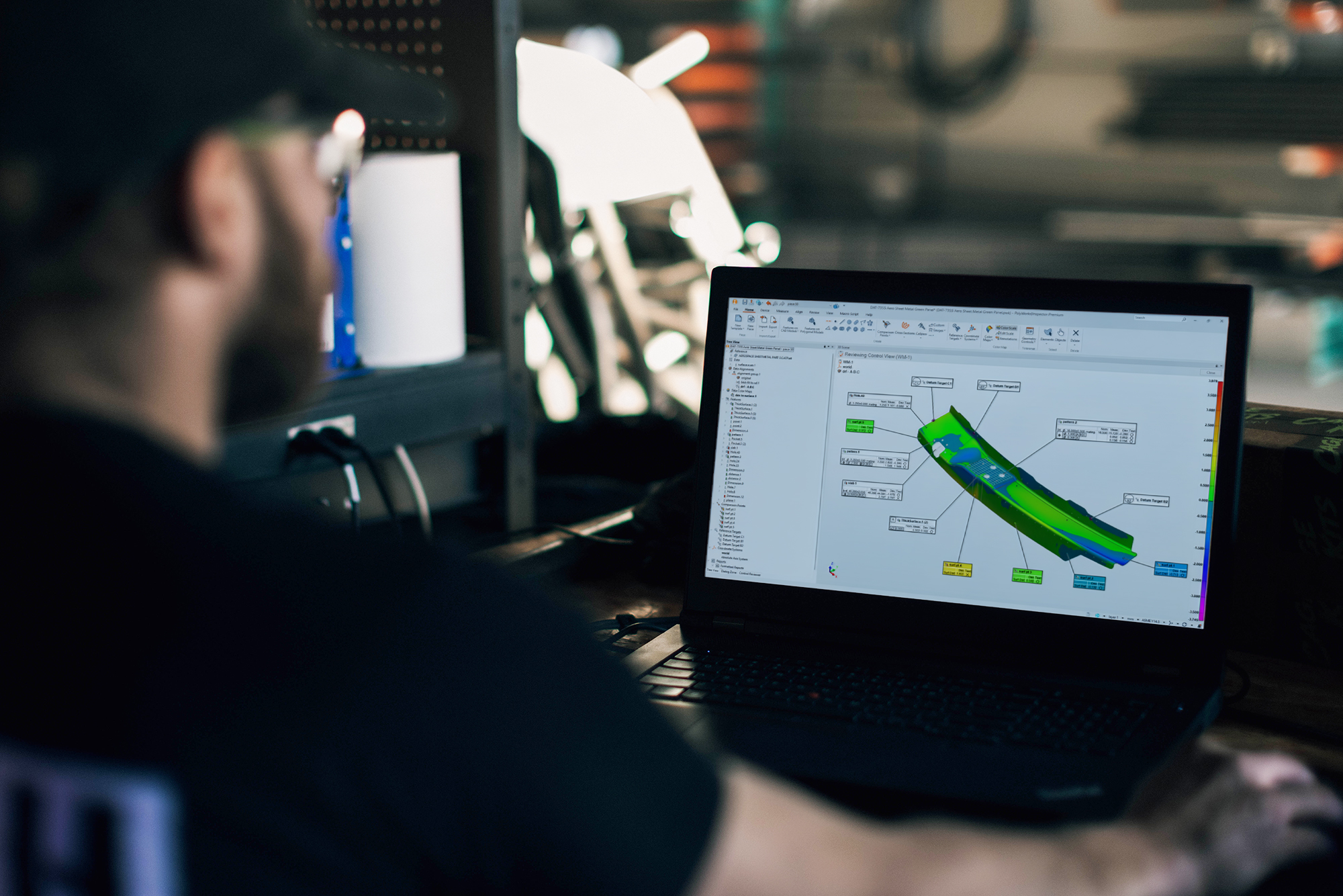 Man sitting in a workshop in front of a computer displaying an aerospace part with a colormap in PolyWorks.