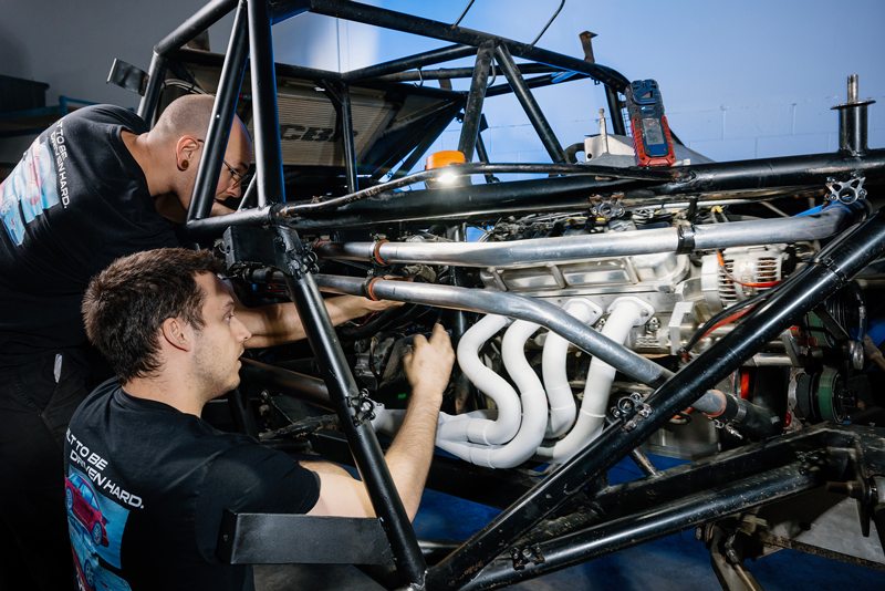 Two EP9 Autosport technicians installing the new manifold on a race car engine inside the vehicle’s chassis.