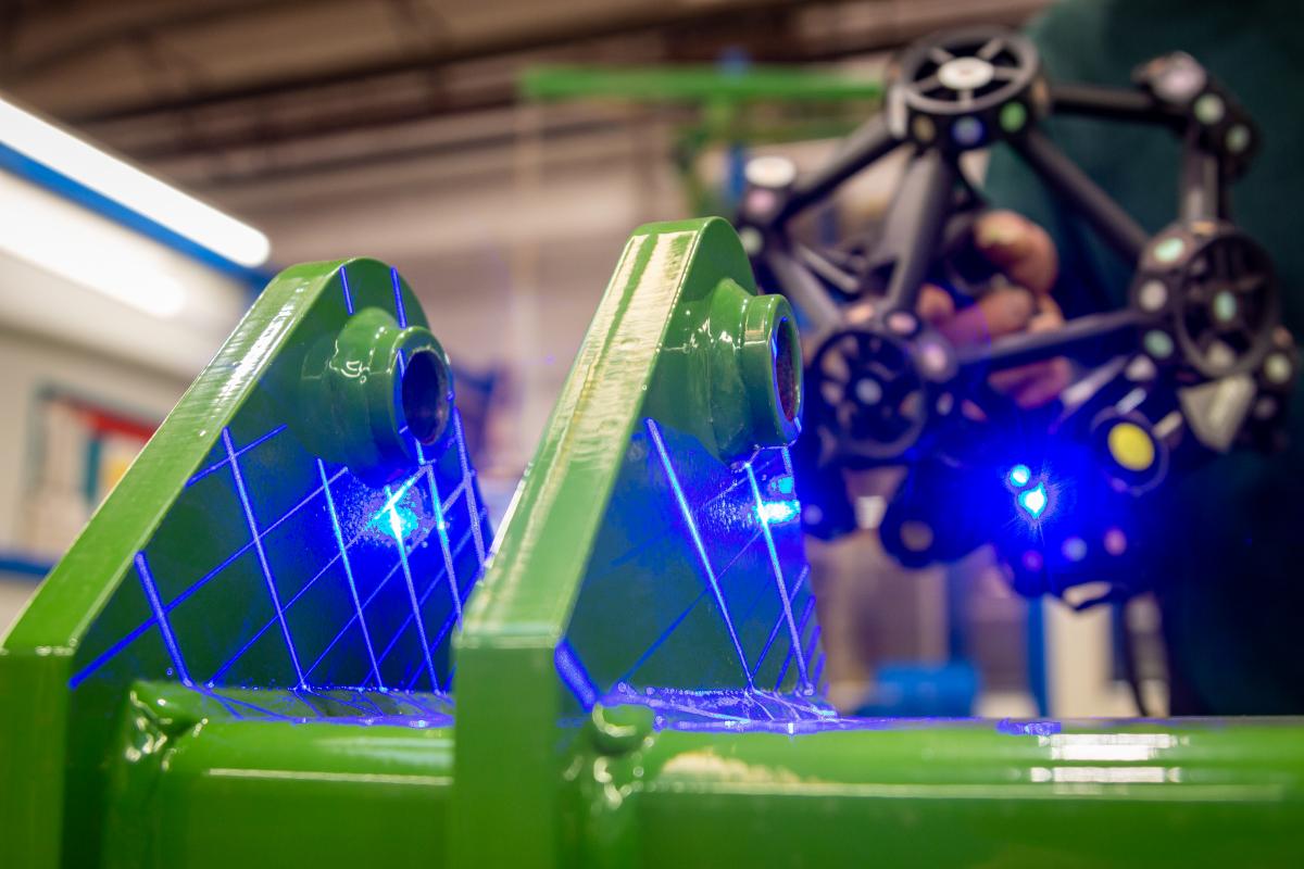 Ein Ingenieur hält ein MetraSCAN 3D, dessen blaue Laserstrahlen auf ein großes glänzendes Teil treffen.
